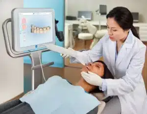 Dentist using an iTero digital scanner to capture a patient’s teeth while a 3D dental scan appears on a monitor.