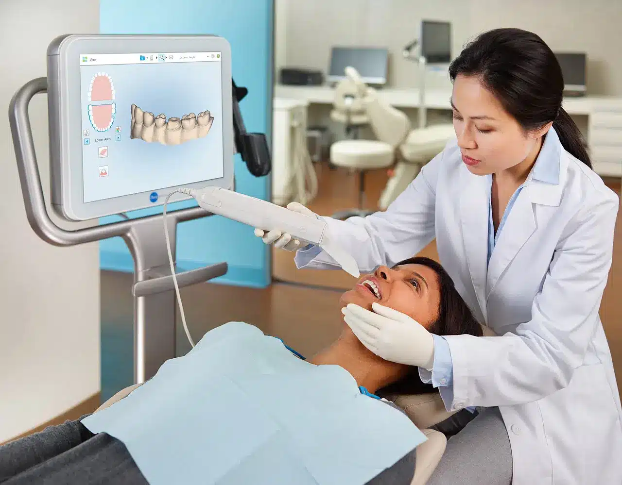 Dentist using an iTero digital scanner to capture a patient’s teeth while a 3D dental scan appears on a monitor.